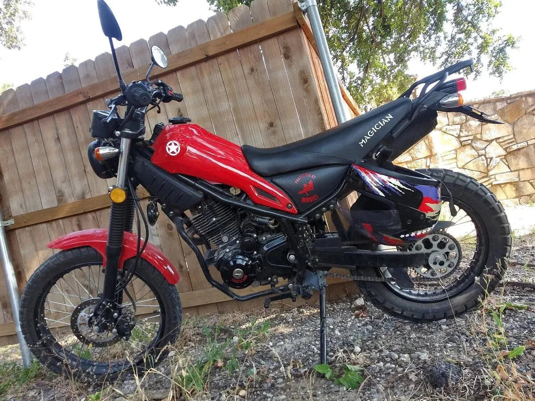 Red and black dirt bike motorcycle with off-road tires parked beside a wooden fence outdoors