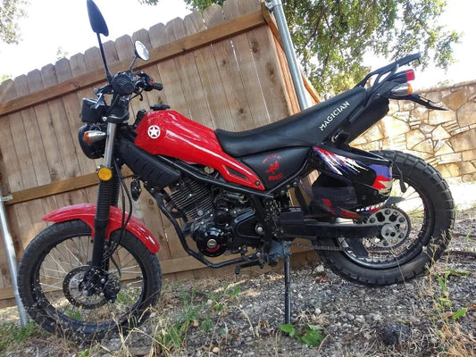 Red and black dirt bike motorcycle with off-road tires parked beside a wooden fence outdoors
