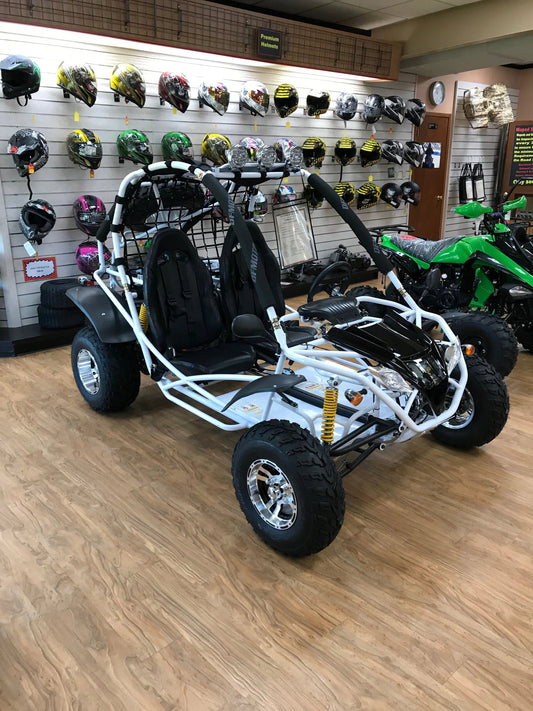 Two-seater go-kart with roll cage on showroom floor, helmets displayed on wall behind.