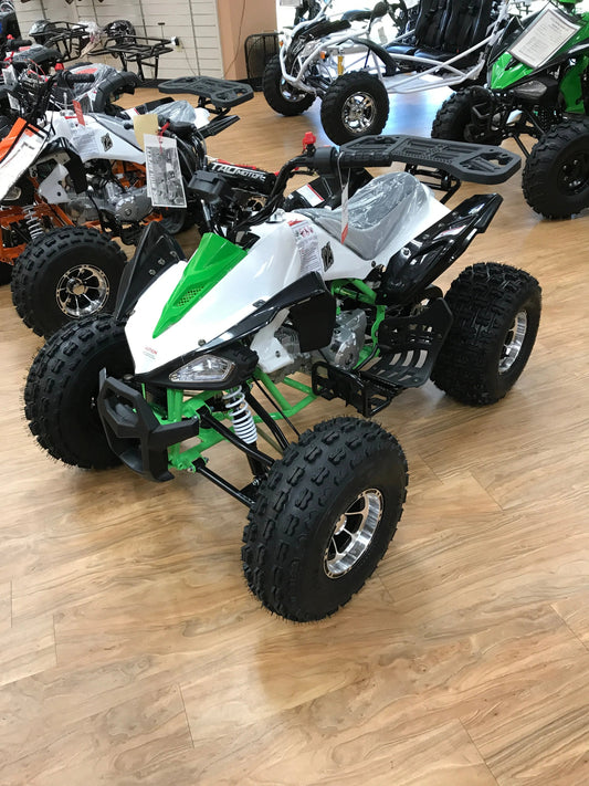 Green and white ATV with off-road tires on display in a showroom with other powersports vehicles.
