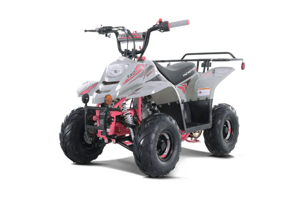 Gray and pink youth ATV with rugged tires, front headlight, and rear cargo rack on white background.