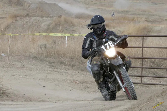 Rider in full gear racing a dirt bike with number 178 on a dusty off-road trail