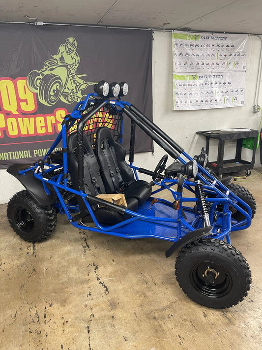 Blue off-road go-kart with roll cage and spotlights, parked indoors on concrete floor
