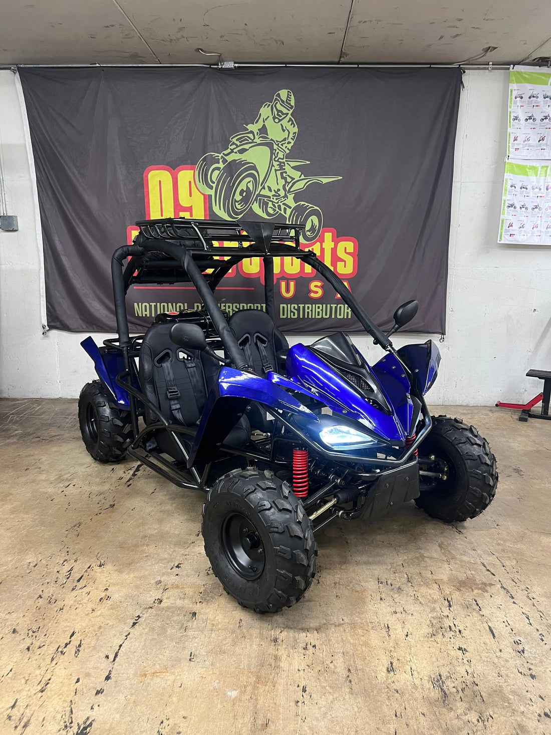 Blue off-road go-kart with roll cage and rugged tires in indoor showroom