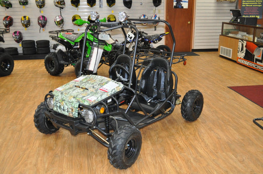 Beginner go-kart with camouflage hood, dual seats and roll cage in a showroom with ATVs and helmets