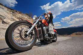 Man riding a motorcycle on a scenic mountain highway under a blue sky
