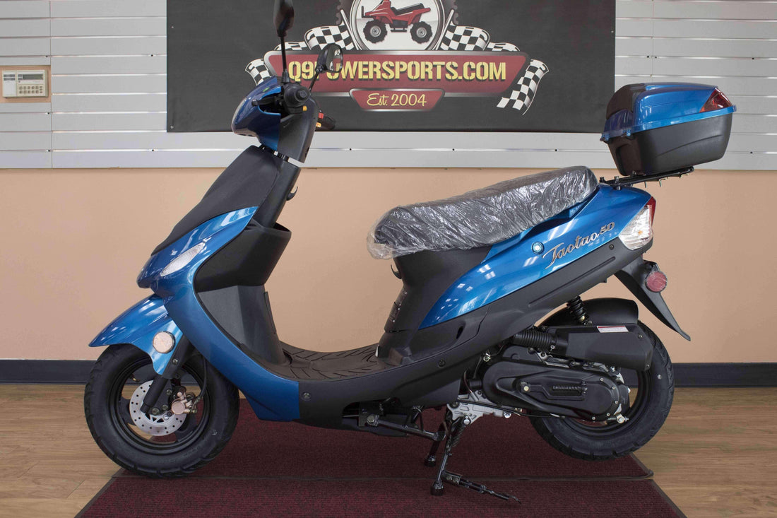Blue 50cc gas powered scooter with rear storage box on showroom floor