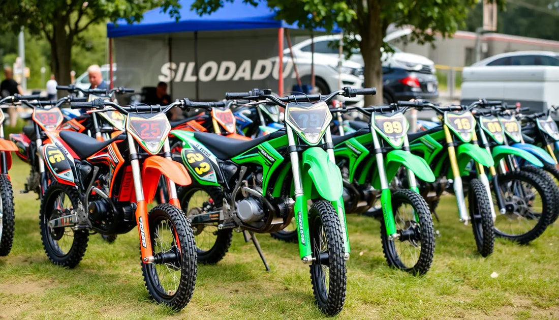 Colorful youth dirt bikes with race numbers lined up outdoors on grass at an event.