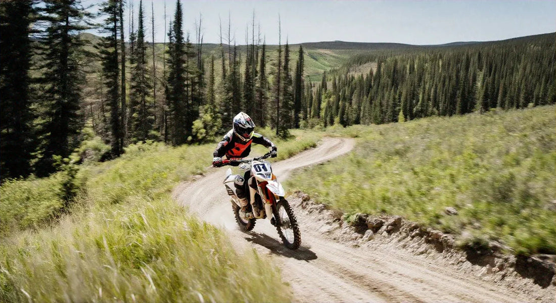 Dirt bike rider on a winding trail in a forested mountain landscape