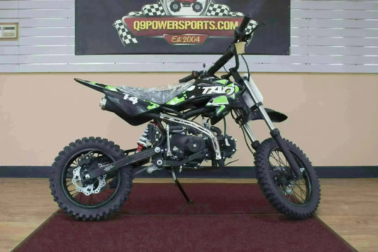 Black and green youth dirt bike with knobby tires displayed indoors on a red mat