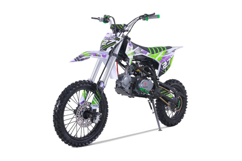 Youth dirt bike with green, purple, and white graphics, rugged tires, and kickstand