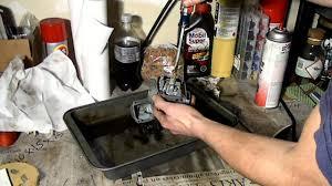 Person cleaning a carburetor on a workbench with brake cleaner and tools nearby
