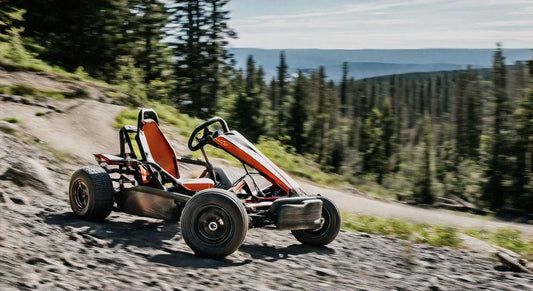 Off-road go-kart with orange accents driving on a rocky mountain trail with forest background