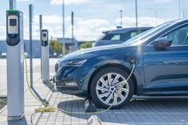 Electric car charging at outdoor charging station, bright day, close-up of front wheel and cable.