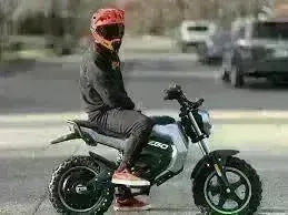 Rider in helmet sitting on a 56V electric mini bike outdoors on paved road.