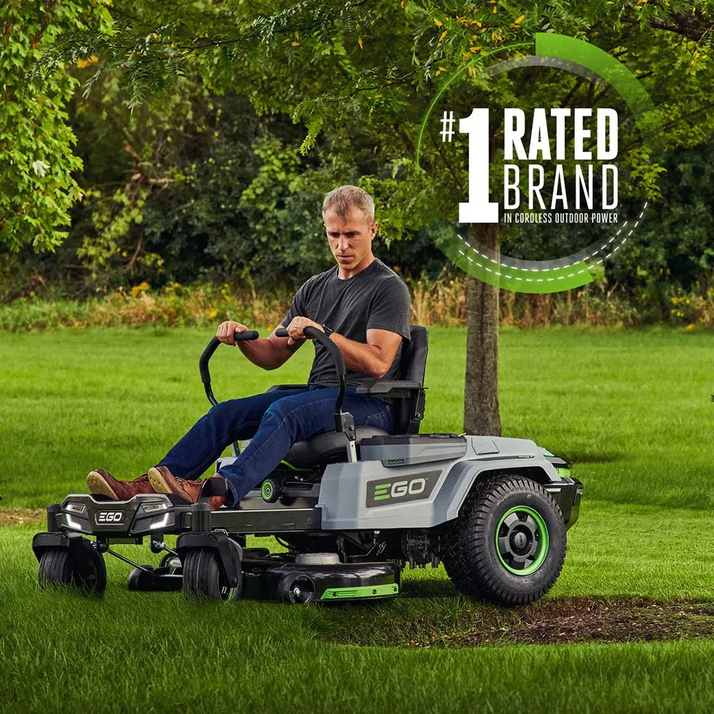 Man riding zero turn electric lawn mower on green grass in a landscaped yard
