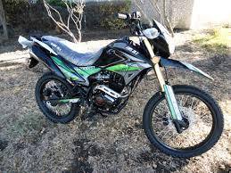 Dual sport motorcycle with black and green accents parked outdoors on grass