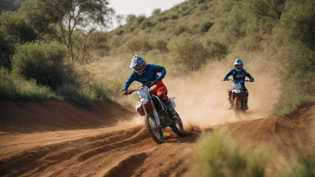 Two riders on dirt bikes racing on an off-road trail, kicking up dust in a green outdoor setting.