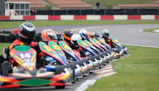 Go-karts lined up on outdoor race track, drivers in colorful helmets ready to race