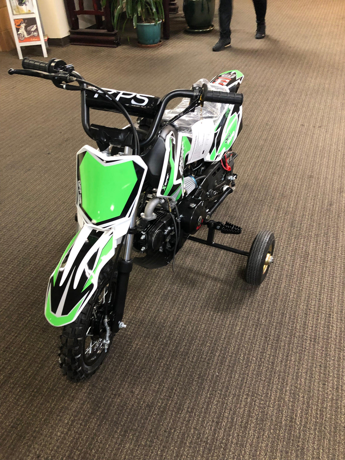 Green 70cc beginner dirt bike for kids with training wheels on indoor carpet