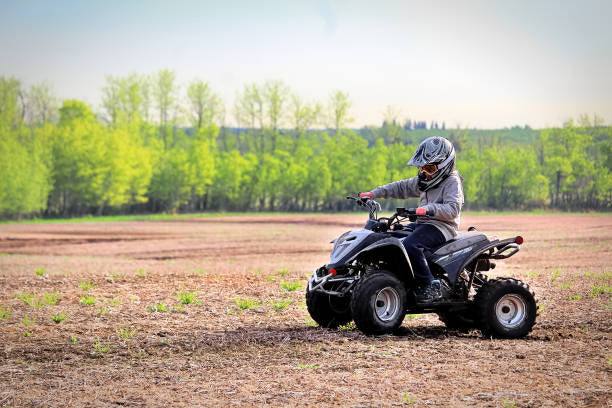 Child riding a gas-powered ATV on a dirt field with trees in the background