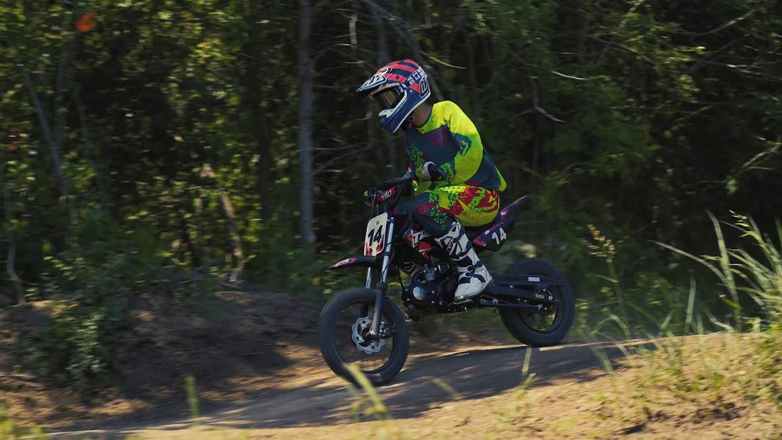 Youth riding gas powered dirt bike on off-road trail, wearing helmet and motocross gear