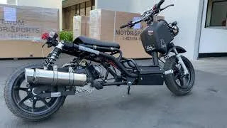 Black scooter with exposed frame and oversized exhaust parked outdoors near shipping boxes