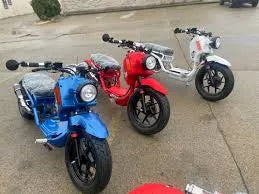 Blue, red, and white 150cc scooters parked outdoors on wet pavement