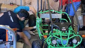 People performing routine maintenance on a green 4-stroke go-kart in a garage.