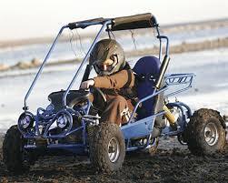Person driving a blue go-kart on rough terrain near water, wearing a helmet.