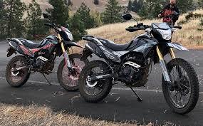 Two dirt bikes parked on a scenic road with trees and hills in the background