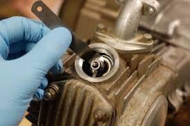 Gloved hand adjusting valve on Chinese ATV engine with feeler gauge tool