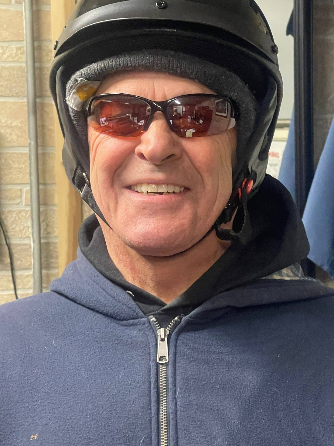 Man wearing a properly fitted motor scooter helmet, sunglasses, and a hoodie indoors