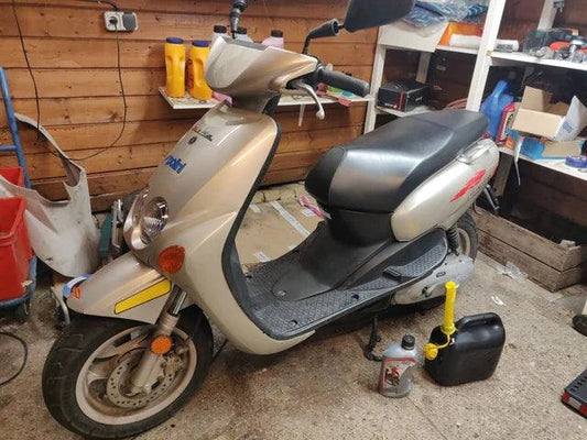 Silver scooter parked in a garage with maintenance tools and supplies nearby