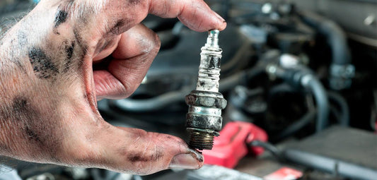 Dirty hand holding a used engine spark plug near ATV or dirt bike engine