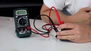 Hand using a digital multimeter to test an ignition coil for ATV or dirt bike troubleshooting