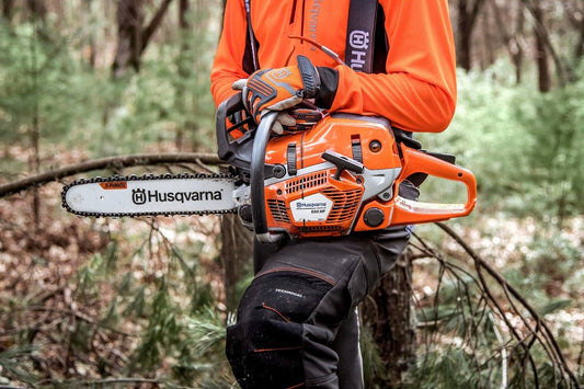 Person in protective gear holding a Husqvarna 550 XP chainsaw outdoors in the woods