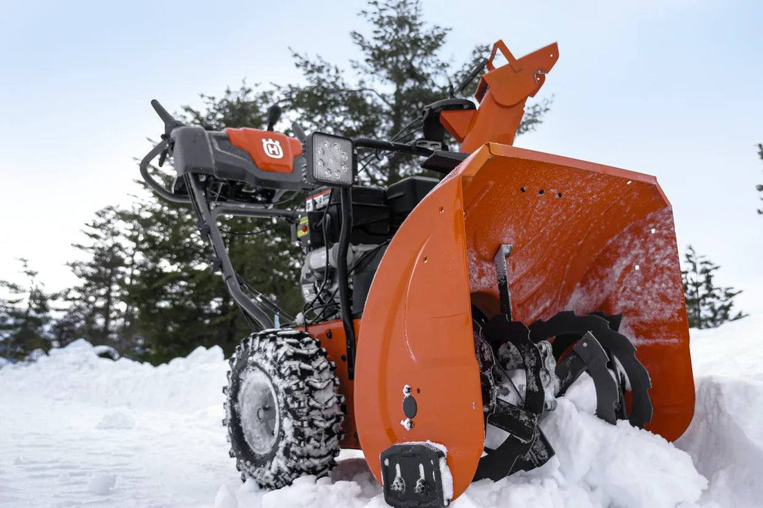 Orange residential snow blower clearing snow outdoors, close-up with snowy trees behind