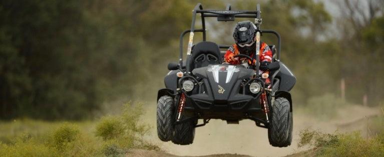 Off-road go-kart with driver wearing helmet, jumping on dirt trail in outdoor setting
