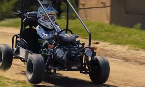 Child wearing helmet driving off-road go-kart on dirt track outdoors