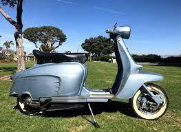 Vintage blue Lambretta scooter parked on grass under sunny sky, classic scooter outdoors