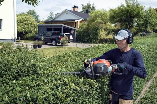 Man using gas-powered hedge trimmer for garden maintenance in residential yard
