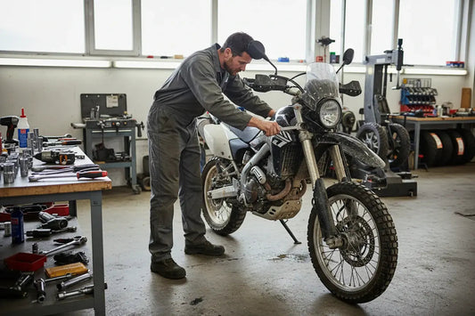Mechanic repairing dual sport motorcycle in workshop with tools and tires in background