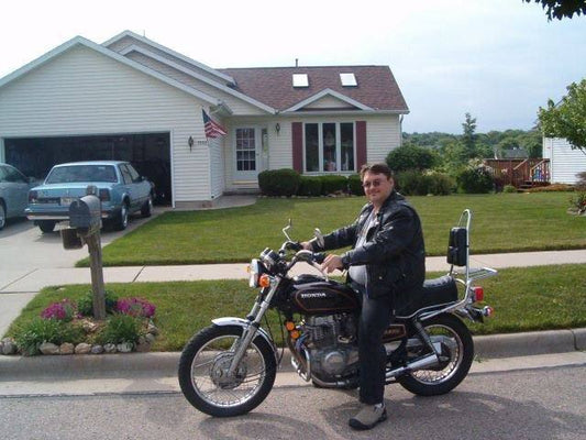 Man in black jacket on Honda motorcycle parked in suburban driveway