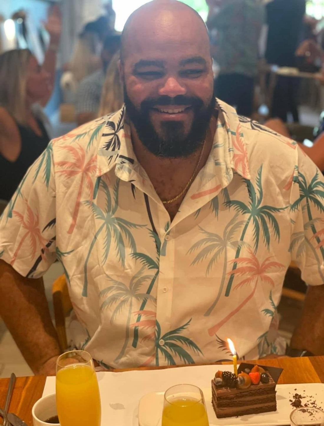 Smiling man in tropical shirt at restaurant with chocolate cake and juice, celebrating occasion