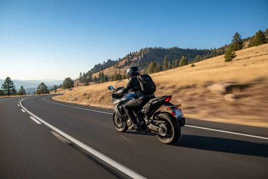 Motorcyclist riding on scenic highway with hills and pine trees under clear blue sky