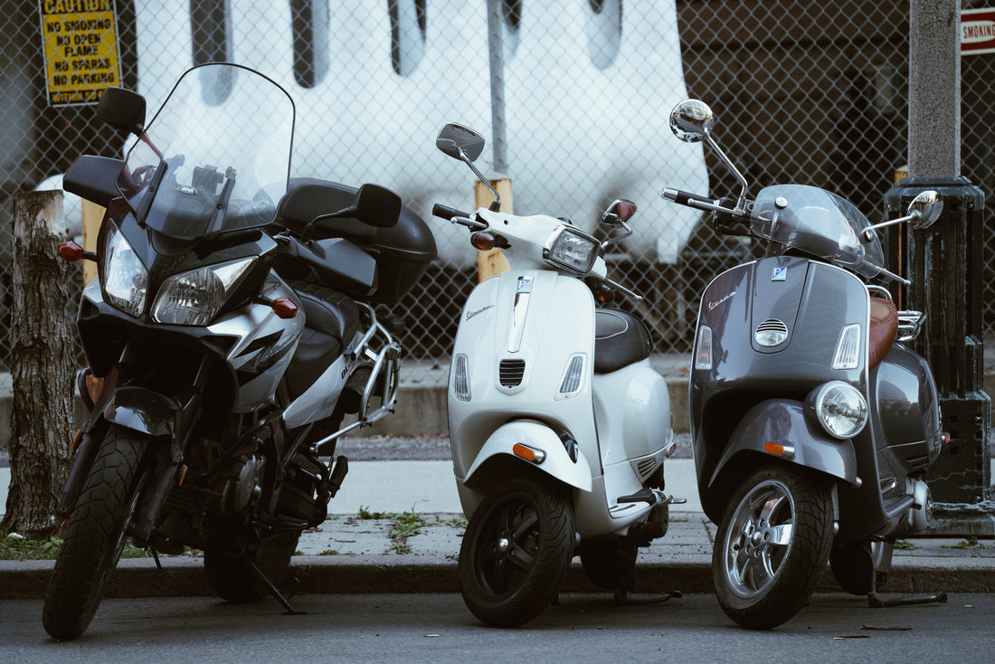 Motorcycle and two scooters parked on city street by chain-link fence