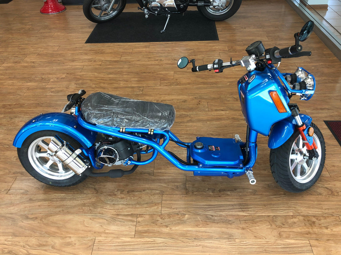 Blue gas-powered scooter with chrome exhaust and alloy rims on showroom floor