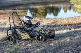 Child driving gas-powered kids go-kart outdoors near a pond on grassy terrain