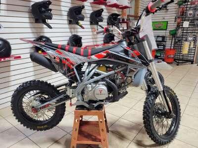 140cc dirt bike with knobby tires on showroom floor, red and black graphics, off-road style